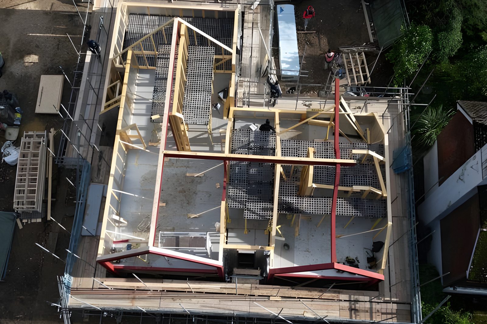 Overhead aerial view of a complex cut roof, showing red steel A frames, steel beams and timber roof members
